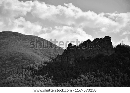 Black and white photo of mountains and rocks. The mountains are covered with dense forests, a small rock rises on top of the hill.