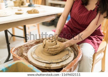 Closeup of messy hands making container of clay on potter's wheel in workshop