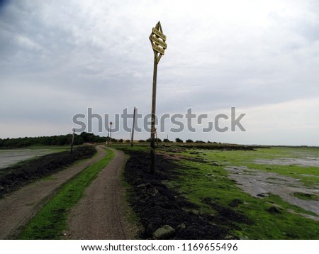 A landscape view of a causeway across a estuary leading to Northey Island in Essex at low tide with a warning sign advising of power cables.