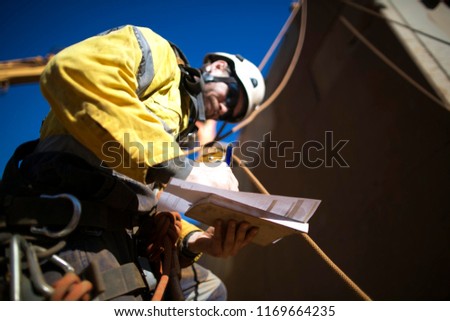 Rope access rigger worker wearing full safety harness, helmet, equipment standing and written crane lifting plan on construction site Perth, Australia  