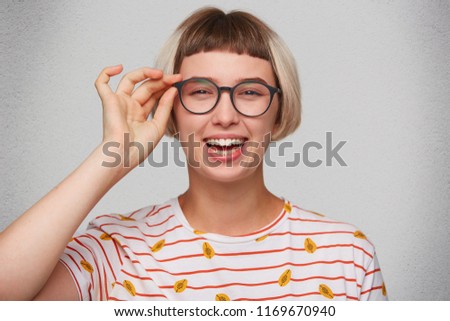 Closeup of happy pretty young woman wears striped t shirt and spectacles feels relxed, laughing and looks directly in camera isolated over white background