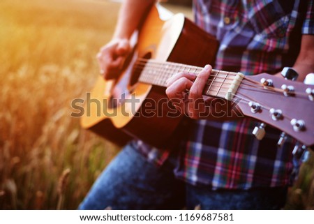 Musician playing guitar at sunset field. Hands, guitar closeup