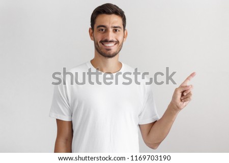 Young man in white t-shirt pointing right with his finger isolated on gray background