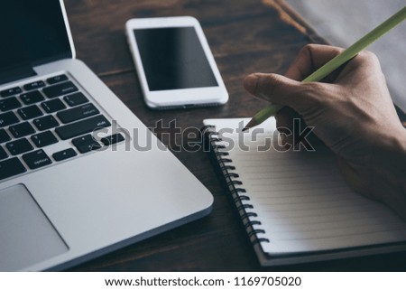 business women hand using pen writing information on paper at workspace with laptop computer,mobilephone on desk in office.people note content diary in notepad placed on wooden desktop with item