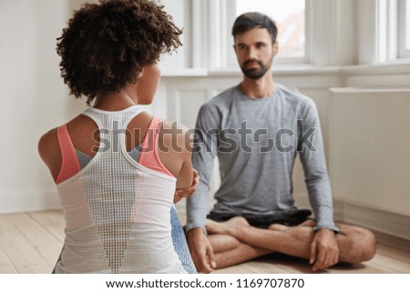 Back view of dark skinned girl and her boyfriend sit in lotus pose on floor opposite each other, have pleasant friendly talk, meditate or practice yoga, try to relax. People and meditation concept