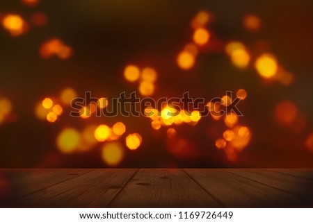 festive background with blurry lights, empty wooden table in foreground with bright candlelight bokeh on dark blurred backdrop, celebration at night concept Royalty-Free Stock Photo #1169726449