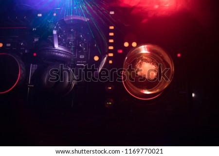 Glass with whisky with ice cube inside on dj controller at nightclub. Dj Console with club drink at music party in nightclub with disco lights. Selective focus
