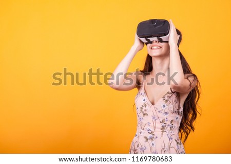 Young girl in virtual augmented reality helmet in studio over yellow background. Testing the application in virtual reality