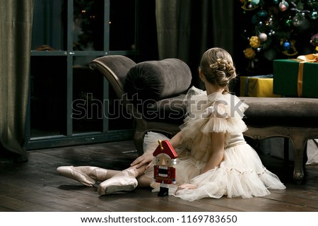 Pretty young ballerina in beautiful tutu with nutcracker in studio, dark background, vintage atmosphere