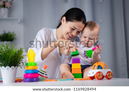 Mom and little son are playing with different developing toys in a bright children's room