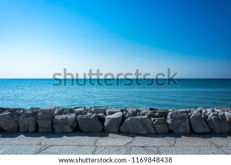 Sea view from a stony beach. Exact horizontal horizon. Blue sea level and strongly enlightened stones coast from the direct sun. Royalty-Free Stock Photo #1169848438