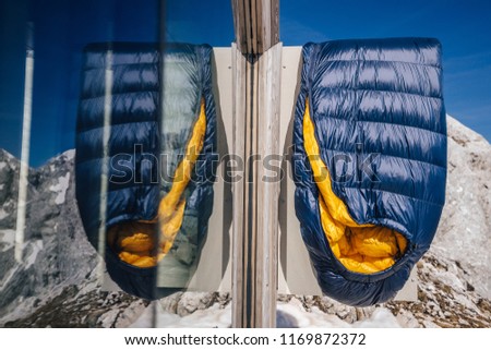 Blue and yellow sleeping bag hanging on the door of a bivouac. Background commercial photo of a sleeping bag in the alpine summer mountain landscape.
