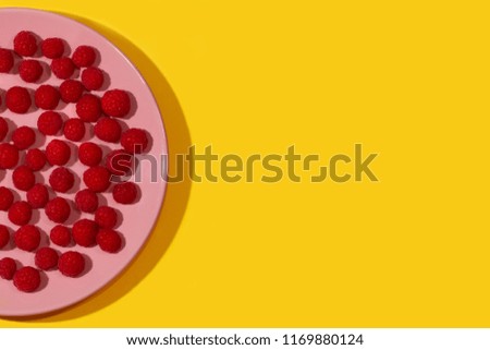 Bright ripe juicy raspberries on a pastel pink plate on a bright yellow background.