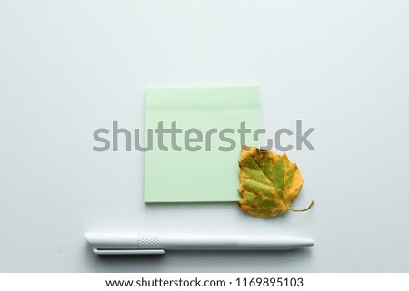 yellow leaf lying on the table, white pen, withered leaf, green notebook for records, autumn background with copy space, for advertising, top view