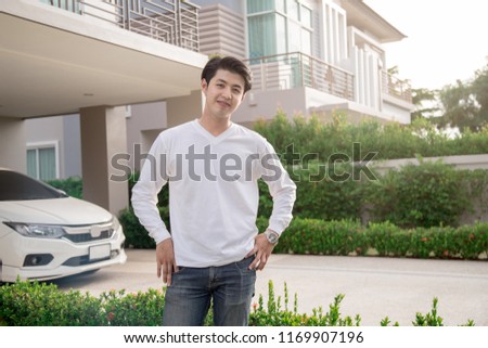 Handsome young man on house background looking at camera. Portrait of laughing young man with hands in pockets. Happy guy smiling.