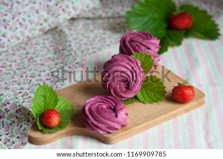 Group of three homemade pink zephyr or marshmallow with strawberries on a wooden board on a woven colorful background