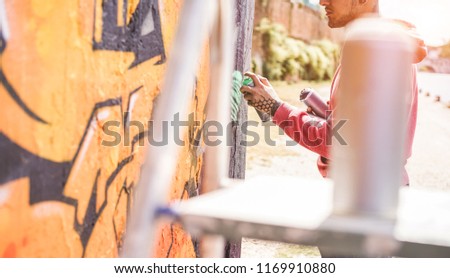 Tattooed graffiti writer painting with color spray his picture on the wall - Contemporary artist at work - Urban lifestyle, youth, millennial generation and street art concept - Focus on hand, can