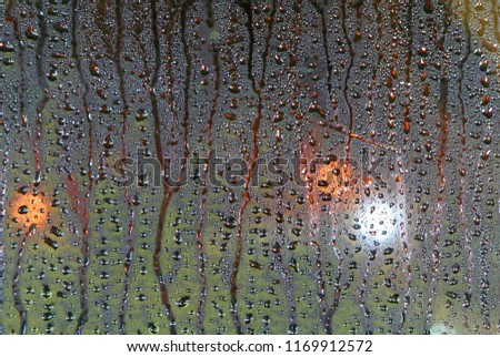 Drops of rain on wet glass window background. Street Bokeh Lights Out Of Focus.