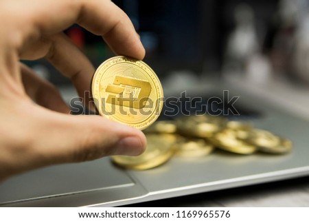 Male businessman hand holding Dash coin on a background of laptop keyboard and pile of golden coins. Virtual money and Financial growth concept. Trading Mining of Dash coin.