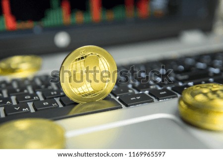 Golden Ripple coin with gold coins lying around on a black keyboard of silver laptop and diagram chart graph on a screen as a background. Mining of ripples online bussiness. Trading.
