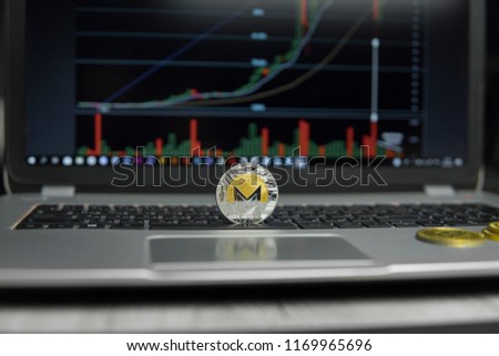 Golden and silver coin of Monero on a black keyboard of silver laptop and diagram chart graph on a screen as a background. Cryptocurrency concept. Mining of ethereums online bussiness. Trading.