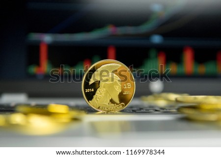 Golden titan bitcoin coin with gold coins lying around on a silver keyboard of laptop and diagram chart graph on a screen as a background. Mining of bitcoins online bussiness. Titans trading.
