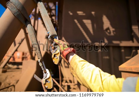 Rope access hand wearing a glove commencing clipping locking carabiner  into 2 tone green safety sling which its had attached on beam structure as abseiling anchor point construction, Australia    