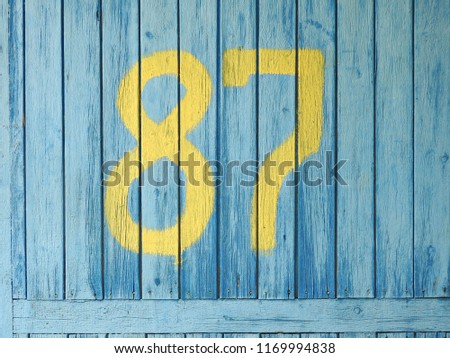 
Yellow numbers eighty-seven, painted on blue wooden boards.					