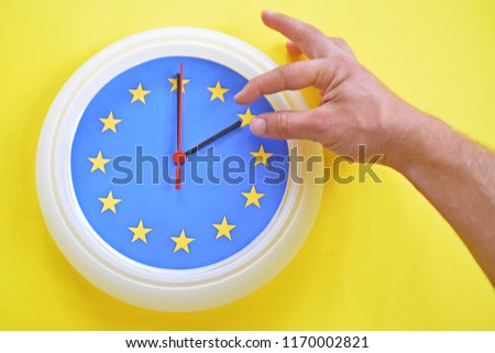 Close-up - a hand continues a clock with the colors of the EU flag for an hour - depicting the time change in the EU, as well as the vote on its abolition Royalty-Free Stock Photo #1170002821
