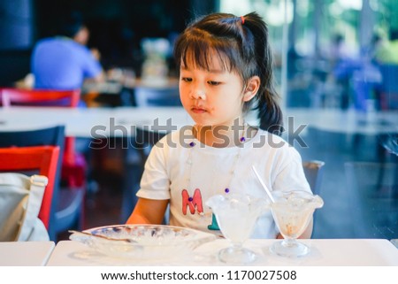 Close up portrait of a hungry greedy little girl eating ice cream sundae in ice cream restaurant.