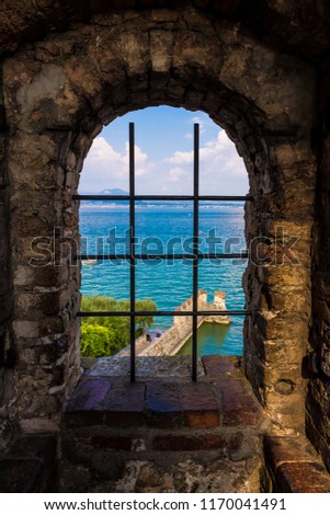 Sirmione seen through a grate window in the scaligero castel, a beautiful medieval picture of sea and land on the Garda Lake