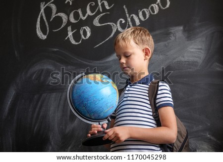European boy with physical globe on black school Board background with English inscription back to school