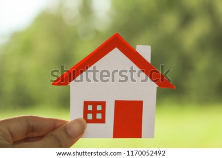 Hand holding Paper cut of house red roof on green background.