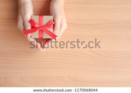 female hands holding a small gift wrapped with red ribbon,gift box on wood table with copy space 