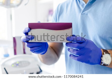 Close up of male dentist holding paper medicine box in hands, with space for text.