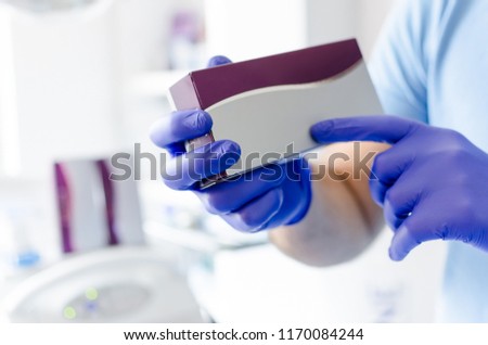 Close up of male dentist holding small medicine box, with space for text.