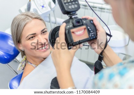 Close up of young female dentist taking picture of satisfied smilling female patient.
