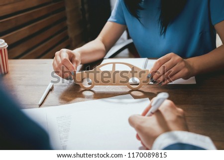 Man signing a car insurance policy, the agent is holding the wooden car model. Car insurance concept.