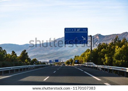 Spanish highway with cars, empty billboards and signs in Andalusian Spain leading to mountains Sierra Nevada on sunset with clear blue sky. Travel and nature concept