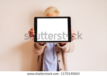 Close up of focus view of tablet with white editable screen . Blurred picture of a woman standing behind tablet and holding it.