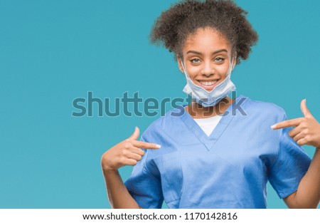 Young afro american doctor woman over isolated background looking confident with smile on face, pointing oneself with fingers proud and happy.