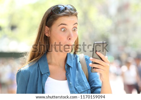 Portrait of an astonished woman reading smart phone content in the street