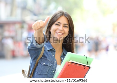 Happy student posing with thumbs up looking at you in the street