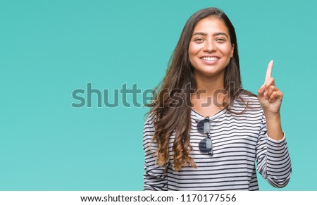 Young beautiful arab woman wearing sunglasses over isolated background showing and pointing up with finger number one while smiling confident and happy. Royalty-Free Stock Photo #1170177556