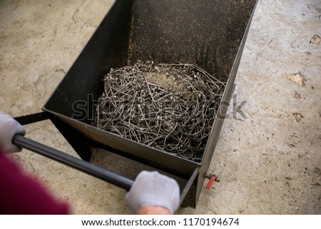 Gloved engineer pushing industrial cart with heap of wires and trash after work