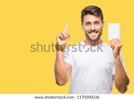 Young handsome man holding notebook over isolated background surprised with an idea or question pointing finger with happy face, number one