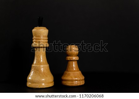 Wooden chess pieces: white king and pawn isolated on a black background close-up.