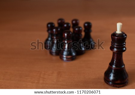 
Wooden figures of a black king and pawns on a brown table close-up.