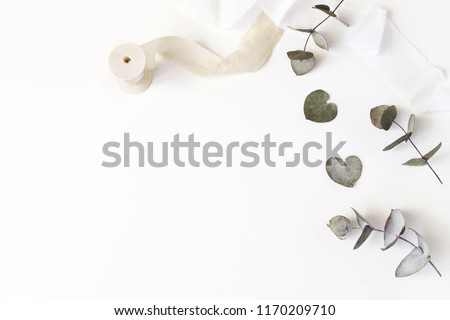 Feminine wedding desktop scene. Composition of dry silver dollar eucalyptus leaves and silk ribbons on white table background. Flat lay, top view.