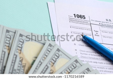 1065 tax form lies near hundred dollar bills and blue pen on a light blue background. US Return for parentship income Royalty-Free Stock Photo #1170216589